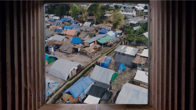 Aerial view through a window frame of a dense refugee camp with tarp-roofed shelters