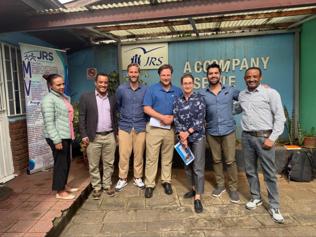 Seven people pose together outside a JRS office building with a corrugated metal facade
