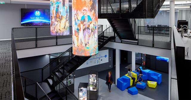 Modern multi-level retail interior with black staircases, colorful art columns and blue seating