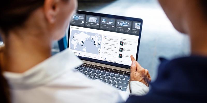 Two people view a logistics dashboard on a laptop showing a world map with shipping routes and data panels.
