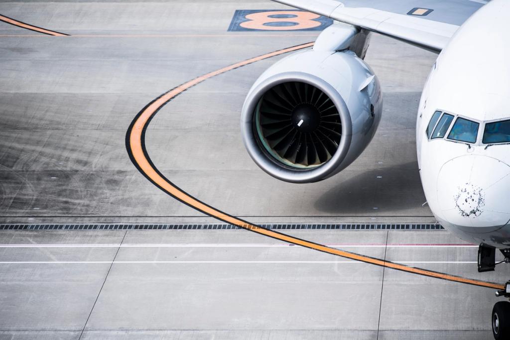 Aerial view of a white passenger jet nose and engine taxiing on airport apron markings