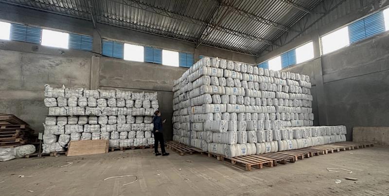 Person standing beside large stacks of white-wrapped aid bales on pallets in a bare warehouse
