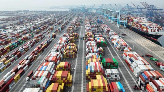 Aerial view of a container port with rows of stacked shipping containers, gantry cranes, and a cargo ship at the dock