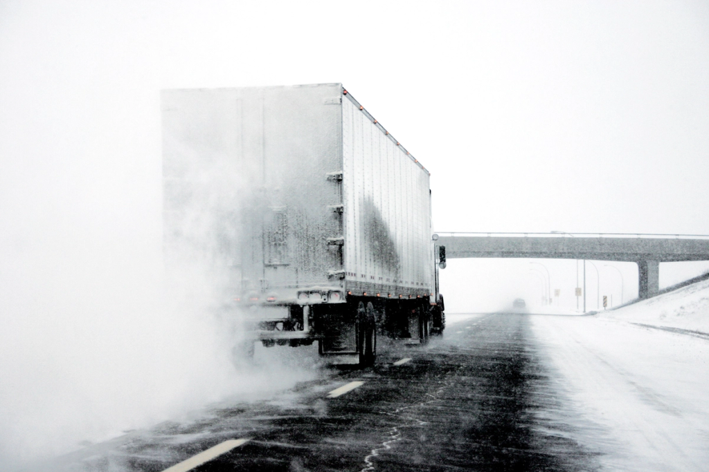 Semi truck spraying water or snow on a highway during winter weather.