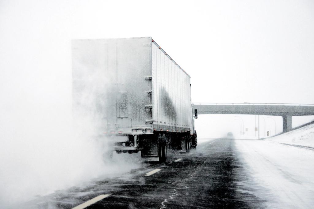 Semi truck spraying water or snow on a highway during winter weather.