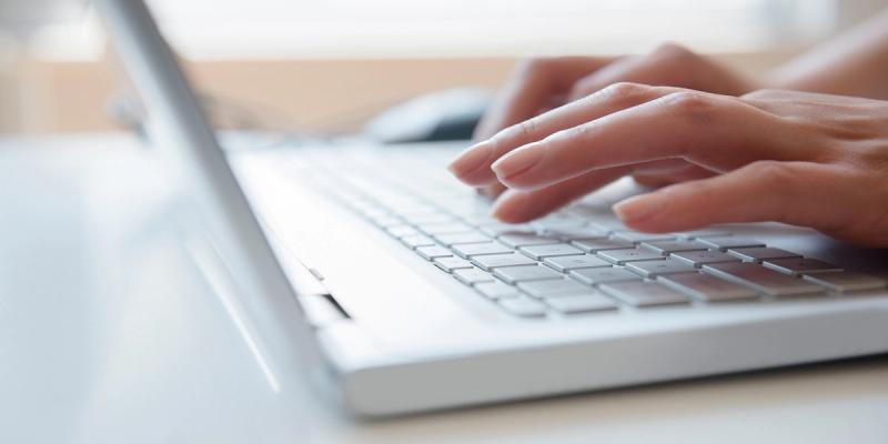 Close-up of hands typing on a white laptop keyboard on a bright desk