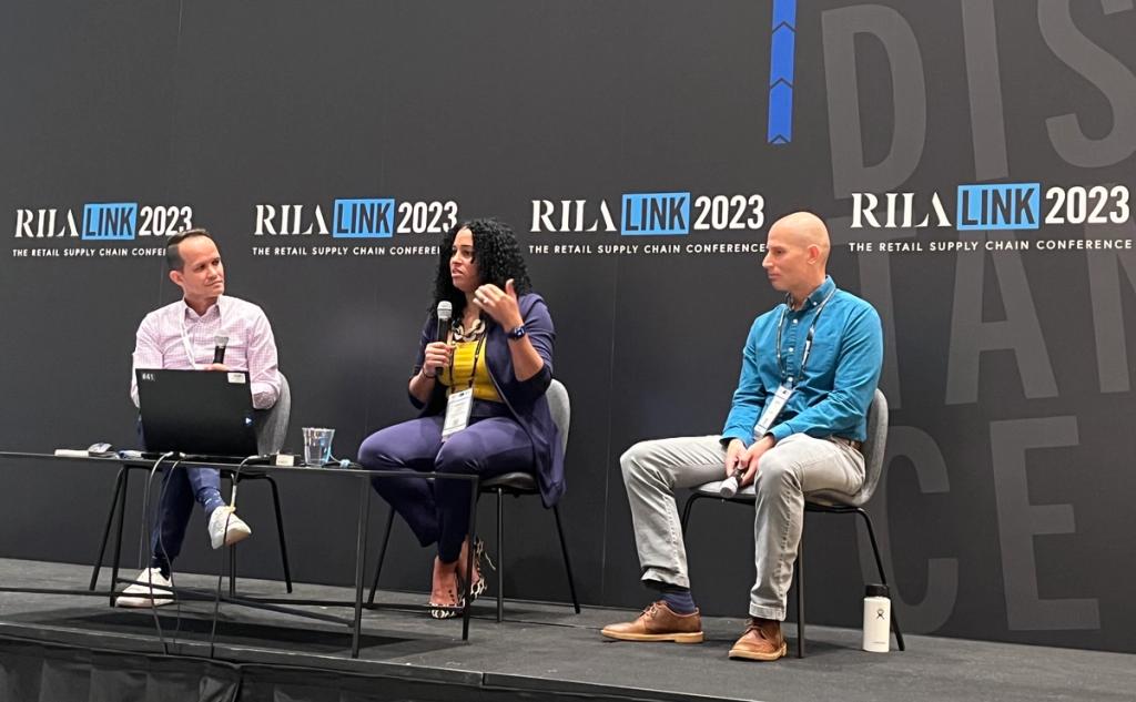 Three panelists seated on stage in front of RILA LINK 2023 backdrops, one speaking into a microphone