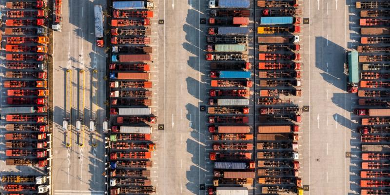 Aerial overhead view of rows of parked trucks with colored container trailers in a yard