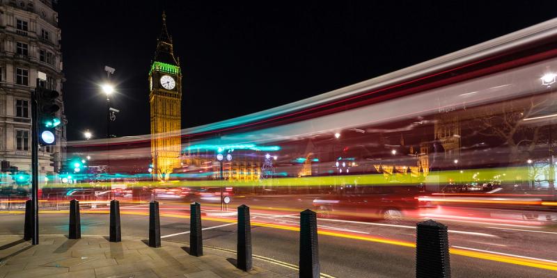 Big Ben lit at night with red and green light trails from passing London traffic streaking across the road