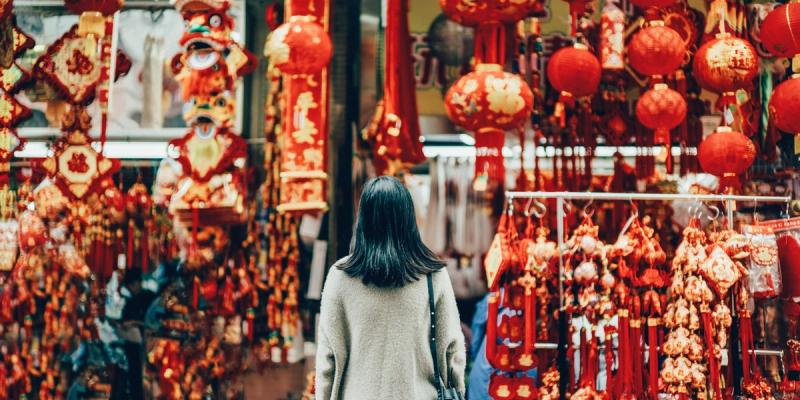 Woman browsing a market stall draped with red Lunar New Year lanterns and decorations