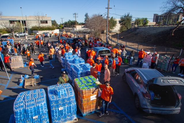 Volunteers in orange shirts loading pallets of bottled water into vehicles in a parking lot