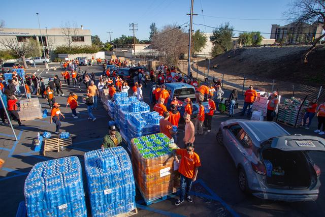 Volunteers in orange shirts loading pallets of bottled water into vehicles in a parking lot