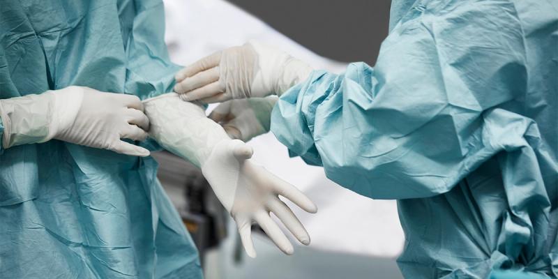 Two people in surgical gowns helping put on white sterile gloves in an operating room