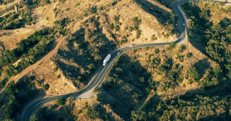 Aerial view of a semi-truck driving along a winding road through dry golden hills