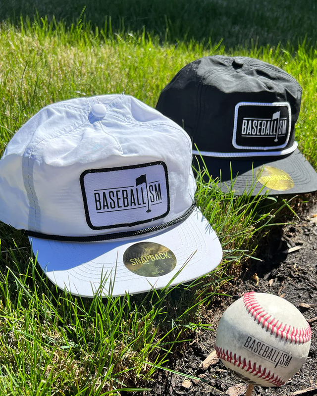 Two Baseballism snapback caps and a baseball resting on grass