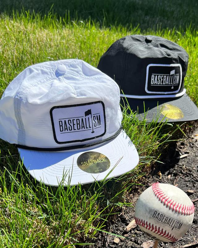 Two Baseballism snapback caps and a baseball resting on grass