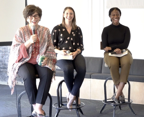 Three women seated on stools holding notebooks during a panel discussion