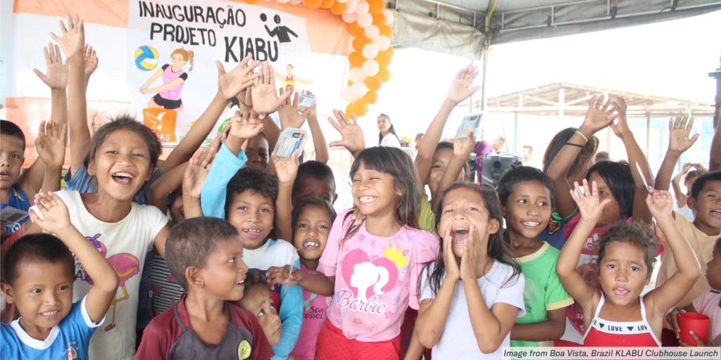 Crowd of smiling children cheering with raised hands at the KLABU clubhouse launch in Boa Vista, Brazil