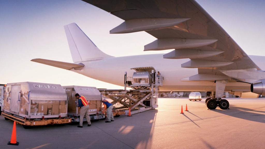 Workers in safety vests load palletized air cargo containers onto a loader beside a wide-body freighter aircraft