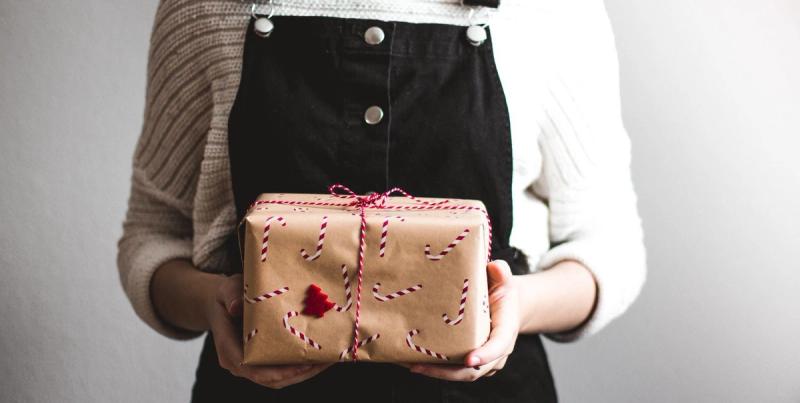 Person in dungarees holding a kraft-paper gift box with candy-cane print tied with red and white string
