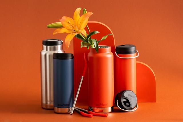 Klean Kanteen stainless steel insulated bottles and tumblers with metal straws and a lily on orange backdrop