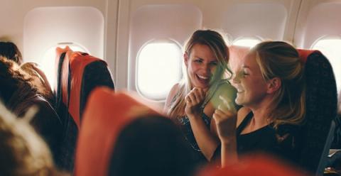 Two women laughing together in airplane seats near the cabin window