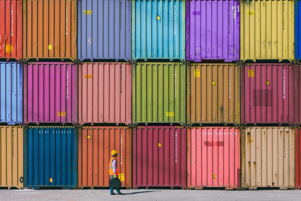 Worker in hard hat walks past a wall of brightly colored stacked shipping containers.