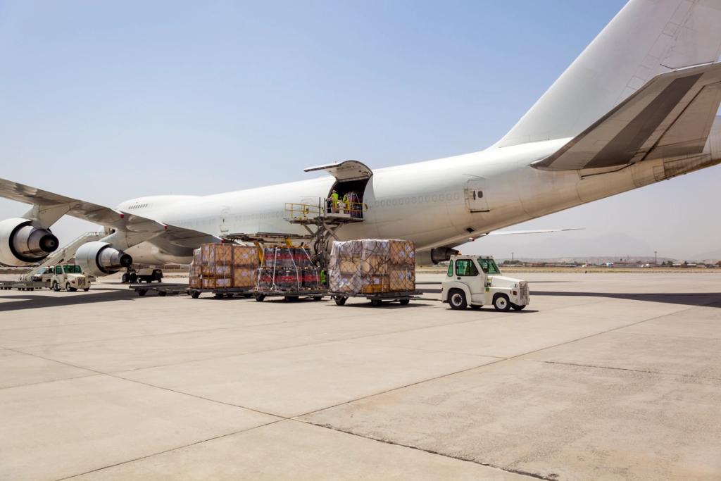 Cargo pallets being loaded into the side door of a parked freighter aircraft with a tug on the tarmac