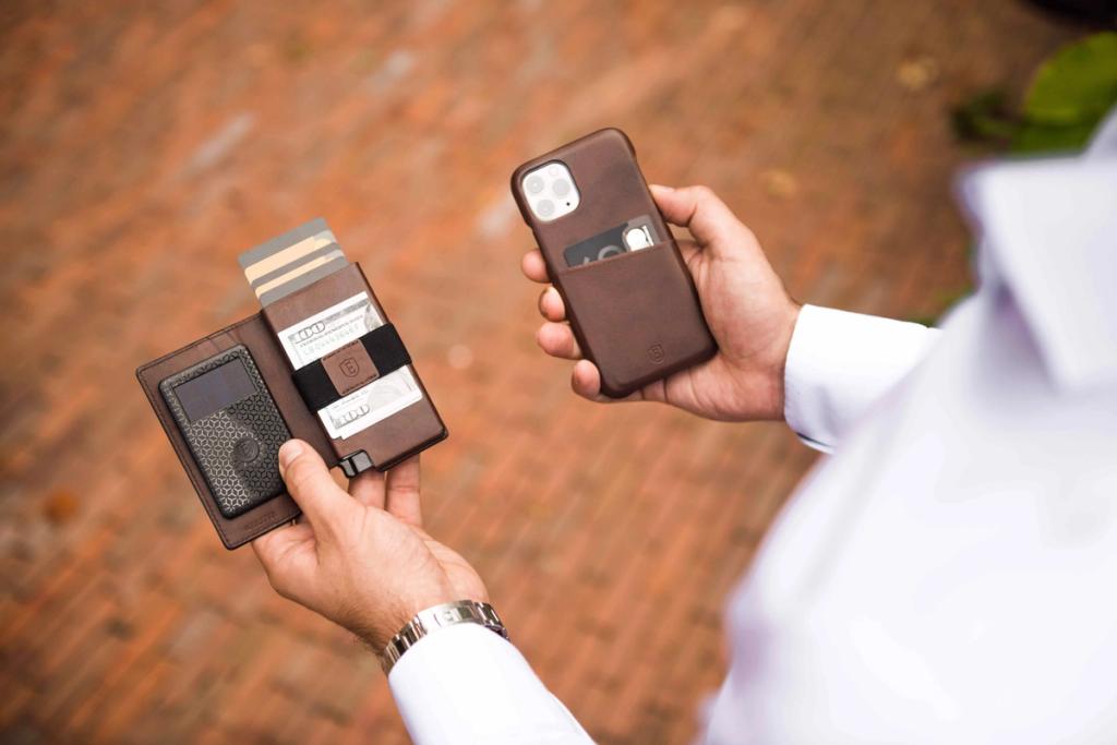 Man holding an Ekster leather cardholder wallet and a brown phone case outdoors