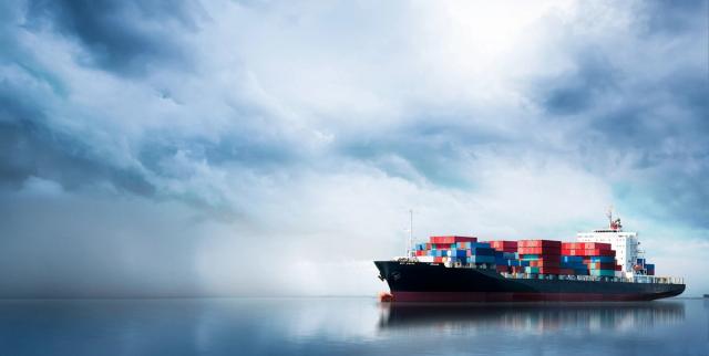 Container ship loaded with cargo on calm water under a dramatic cloudy sky