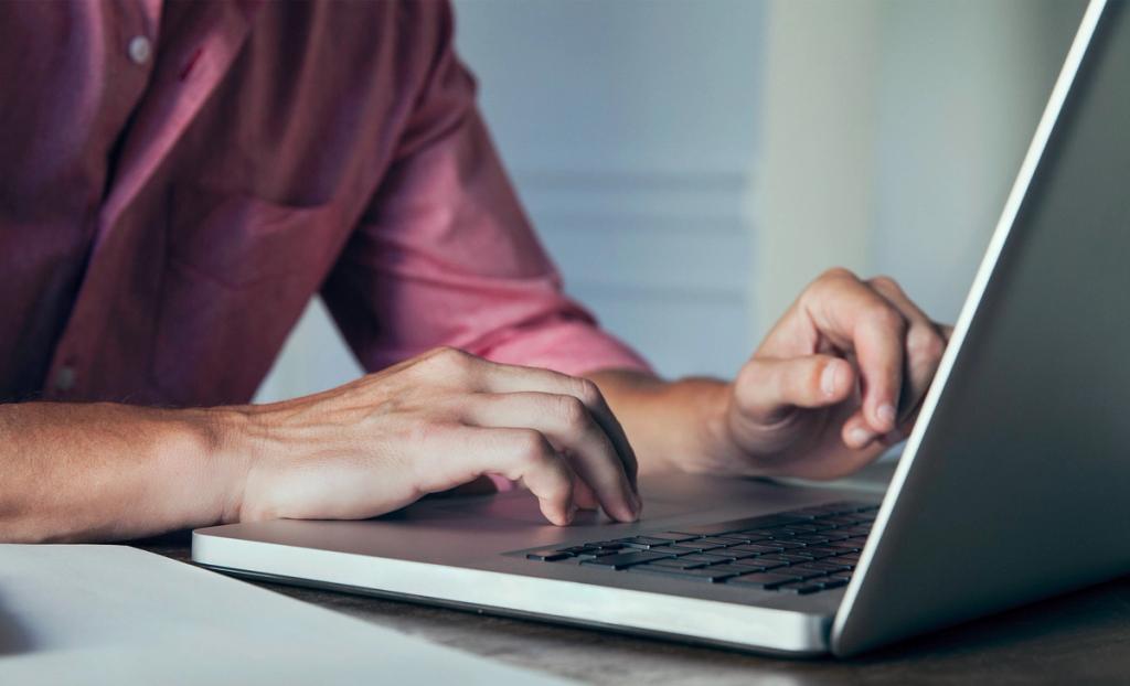 Close-up of a person's hands typing on a laptop keyboard at a desk