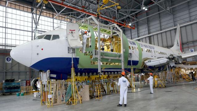 Workers in white coveralls and hard hats converting a passenger jet to cargo in an aircraft maintenance hangar