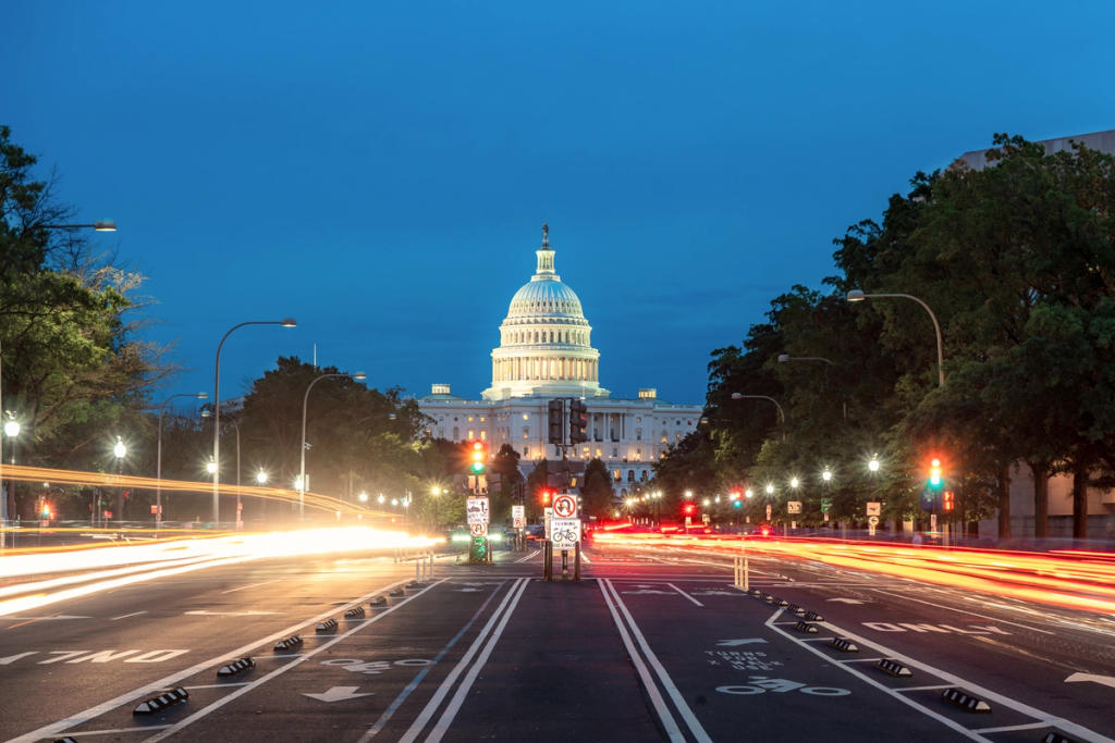 US Capitol dome illuminated at dusk with light trails from traffic streaking down the avenue
