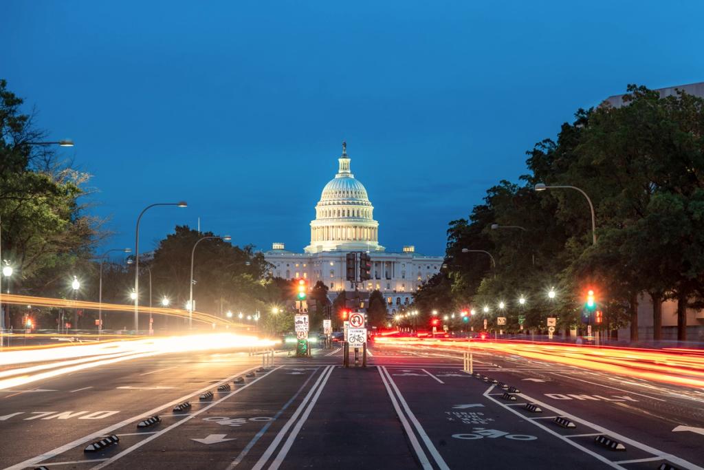 US Capitol dome illuminated at dusk with light trails from traffic streaking down the avenue