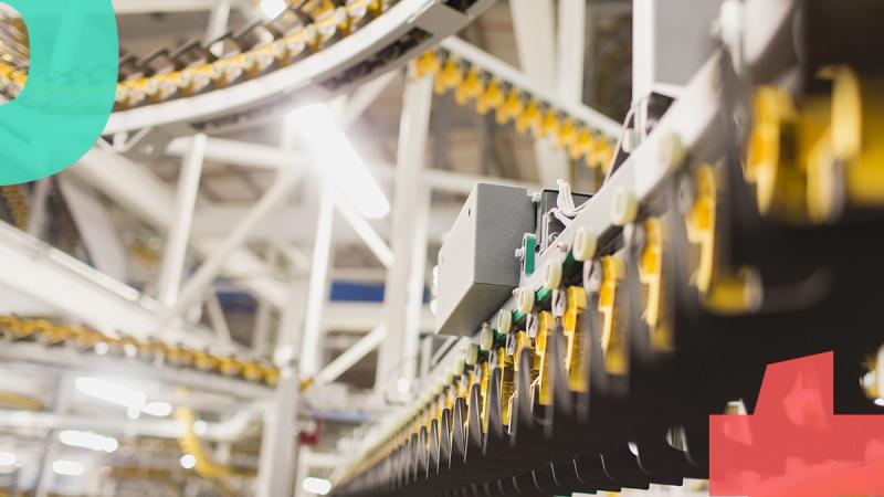 Overhead garment conveyor system with rows of yellow hangers moving through a brightly lit factory