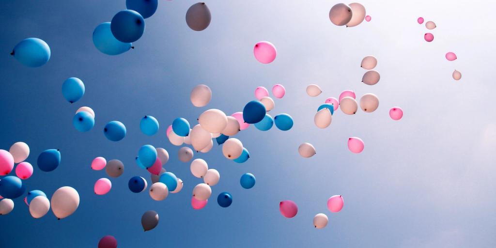 Pink, blue and white balloons floating up into a soft blue sky