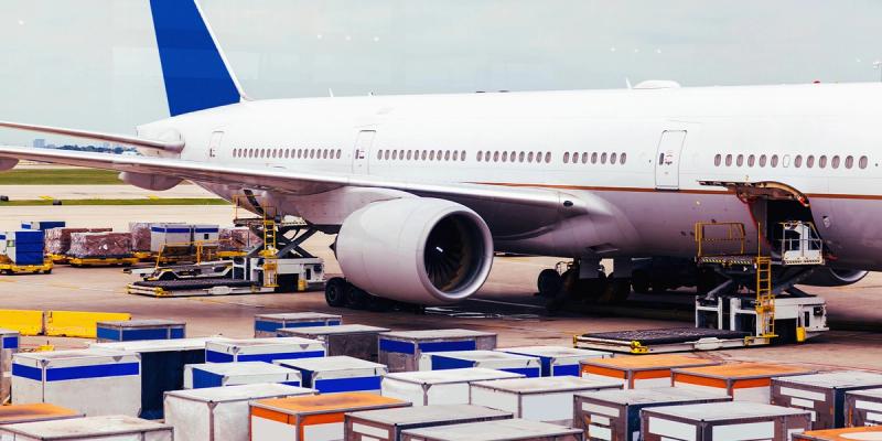 White widebody cargo aircraft on tarmac being loaded, with air cargo containers in the foreground