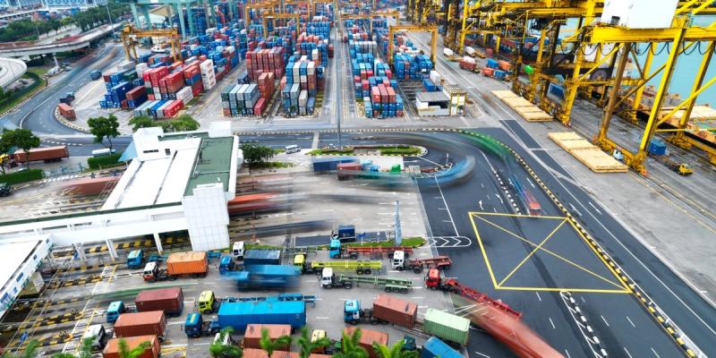 Aerial view of a container port with stacked containers, gantry cranes and trucks on curved roadways