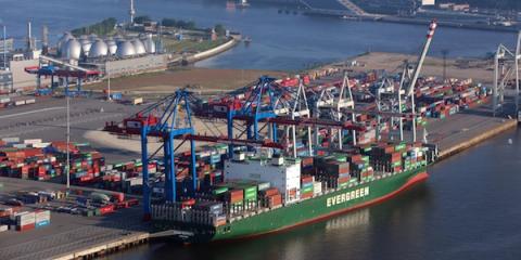 Green Evergreen container ship docked at a port with blue gantry cranes and stacked containers