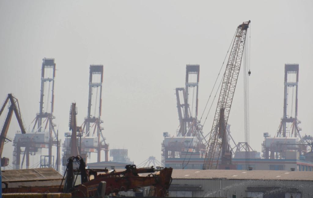 Hazy port skyline of tall gantry cranes and a mobile crane over a container terminal.