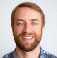 Headshot of a smiling bearded man with light brown hair wearing a patterned blue shirt