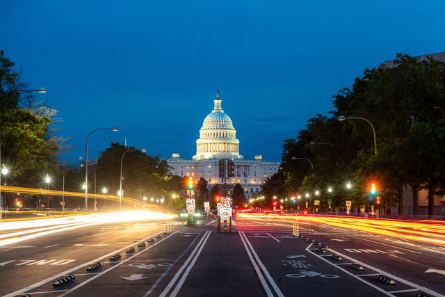US Capitol dome illuminated at dusk with light trails from traffic streaking down the avenue