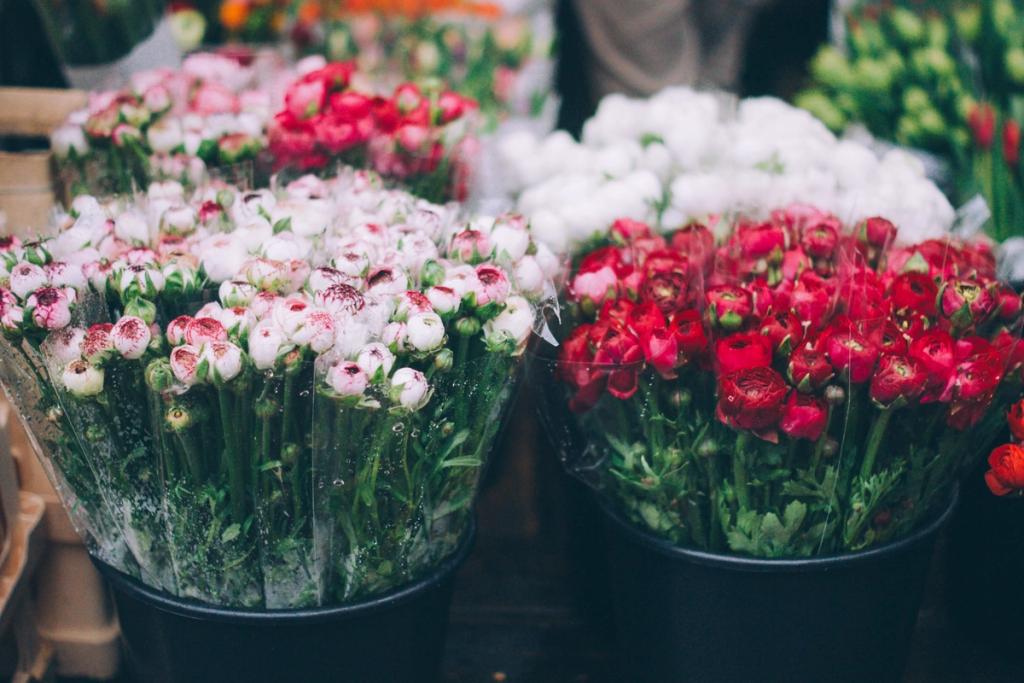 Buckets of wrapped pink, white, and red ranunculus flowers for sale at a market stall
