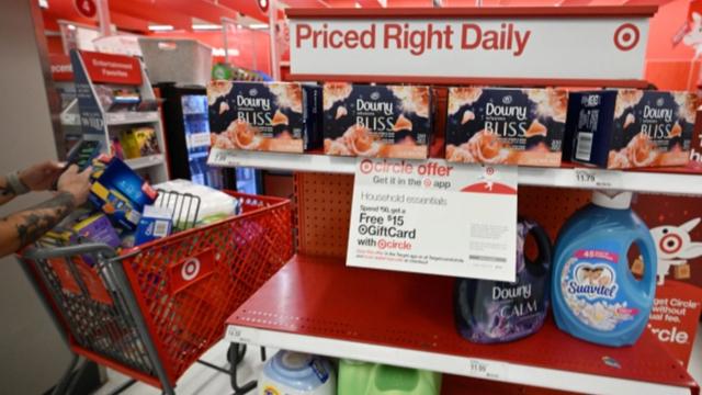 Shopper with a red Target cart browses a store shelf of Downy and Suavitel laundry products under a Priced Right Daily sign