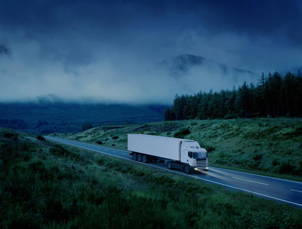 A cargo truck travels along a rural highway through hilly terrain.