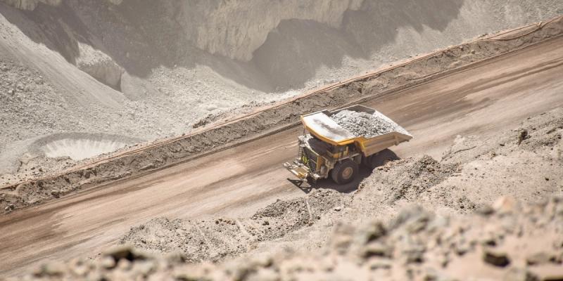 Yellow haul truck loaded with ore driving on a winding road through a grey open-pit mine
