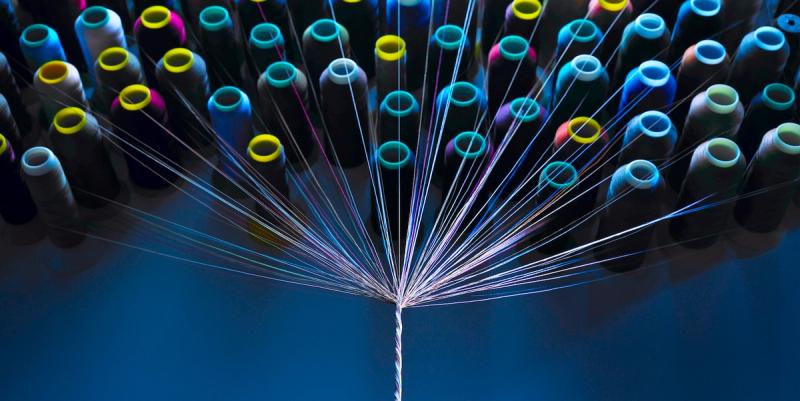 Colorful thread spools fanning many strands to a single point against blue light