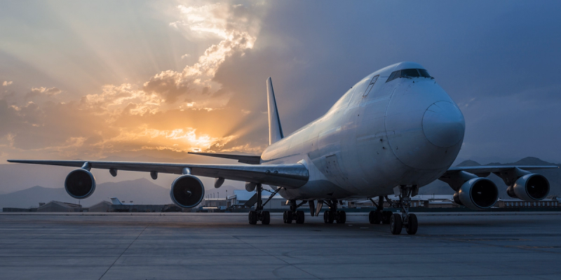 White Boeing 747 freighter parked on a tarmac at sunset with sunburst behind the wing