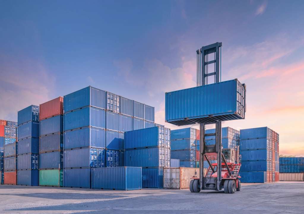 A forklift loads a stacked shipping container in a cargo terminal.