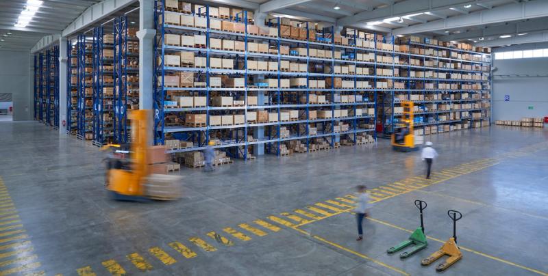 Wide warehouse interior with tall pallet racking, a forklift and blurred workers in motion